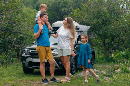 A cheerful and joyful family proudly posing outdoors with a spacious SUV amidst a beautiful lush green settingの写真素材