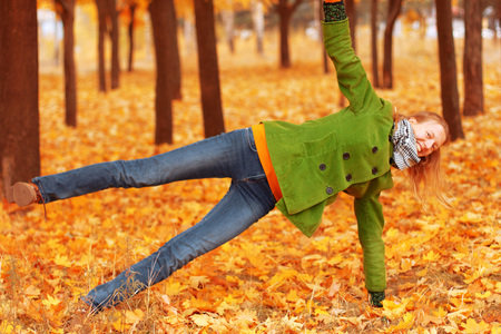 woman in a green jacket practices yoga in the autumn parkの写真素材