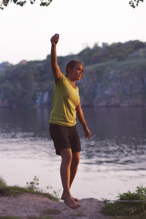 girl walks on Slacklin on the background of the river and the trees