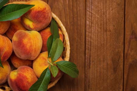 Ripe and beautiful peaches in a basket on a wooden background.の写真素材