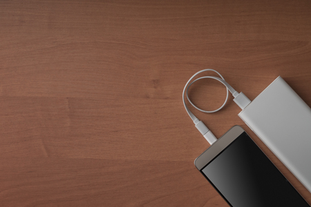 A modern smartphone and a connected power bank on a wooden background.の写真素材