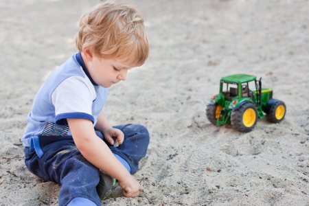 Little toddler boy playing with sand and toy on playground in summerの写真素材
