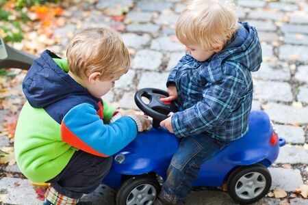 Two toddler boys playing with car in autumn parkの写真素材