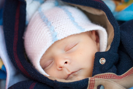 Adorable baby boy in winter clothes sleeping in orange stroller outdoor