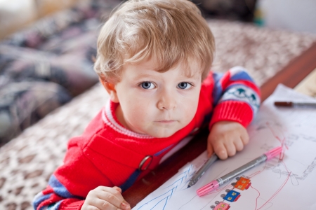 Little toddler boy with blue eyes drawing indoor with colorful pensの写真素材