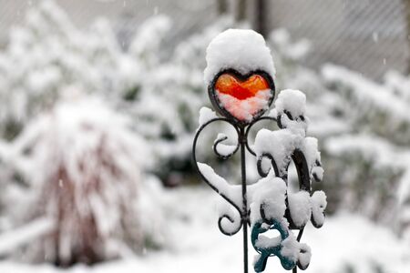 Red iron heart during snowfall in winter gardenの写真素材