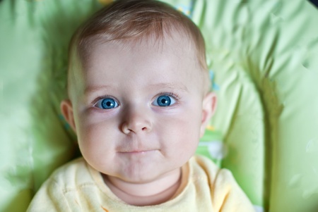 Adorable baby boy with blue eyes sitting in baby chairの写真素材