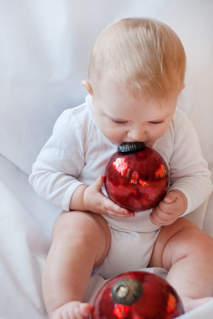 Lovely baby boy playing with Christmas tree balls on white backgroundの写真素材