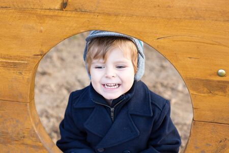 Beautiful toddler boy in blue coat on cold winter day on playgroundの写真素材