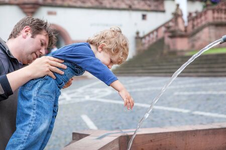 Young father playing with toddler boy in summer city with water of fountainの写真素材