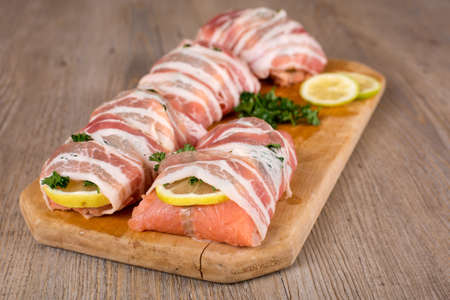 Fresh salmon wrapped with bacon prepared for grill on wooden cutting boardの写真素材