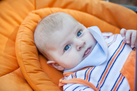 Lovely baby boy outdoor in orange stroller summer