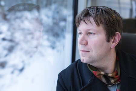 Young man traveling by train and looking out the window outside, while it moving. travelの写真素材