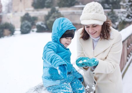 Young mother and little toddler boy having fun with snow outdoors on beautiful winter dayの写真素材