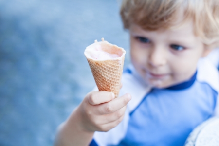 Little toddler boy eating ice cream in cone in summer with focus on ice creamの写真素材