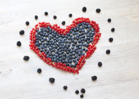 Heart made with red currant berries and blueberries on wooden tableの写真素材