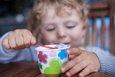 Little blond toddler eating ice cream in self made ice cream cup. Selective focus on ice cup and handsの写真素材