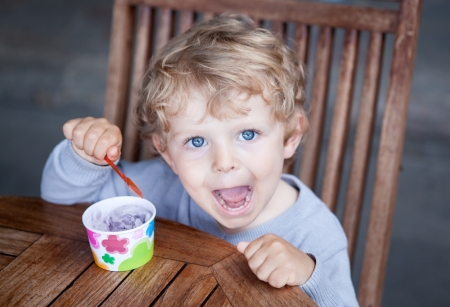 Little blond toddler boy eating ice cream in self made ice cream cupの写真素材