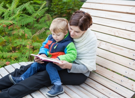 Young mother and toddler reading book in summer parkの写真素材