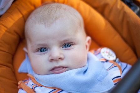 Lovely baby boy outdoor in orange stroller summer