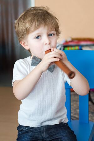 Little adorable boy playing wooden flute indoorの写真素材