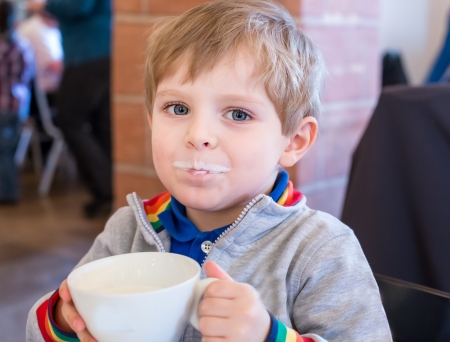 Little toddler boy drinking cup of milk in restaurantの写真素材