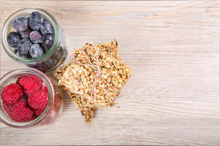 Homemade healthy muesli bars with raspberry and blueberry in jars on wooden textureの写真素材