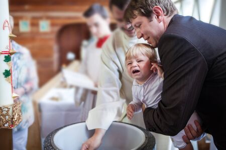 Little baby boy being baptized in catholic church holding by fatherの写真素材