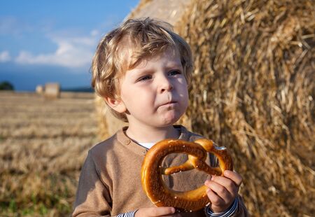 Little boy eating German pretzel on goden hay field in summer.の写真素材