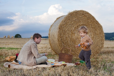 Young man and little toddler boy making evening picnic on hay field, Germany.の写真素材