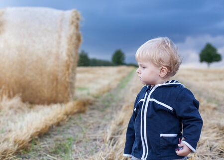Little boy eating German sausage on goden hay field in summer. Selective focus on pretzelの写真素材