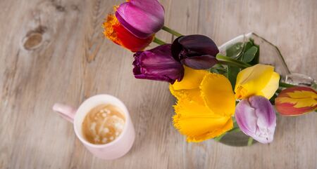 Colorful tulips and a cup of fresh coffee on wooden backgroundの写真素材