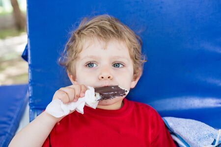 Little blond toddler eating chocolate ice cream, outdoorsの写真素材