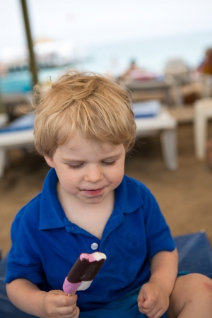 Little blond toddler eating chocolate ice cream, outdoorsの写真素材