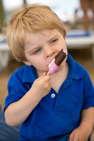 Little blond toddler eating chocolate ice cream, outdoorsの写真素材