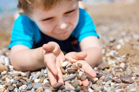 Little toddler boy playing with sand and stones on the beach in summer. Selective focus on stones and hands.の写真素材