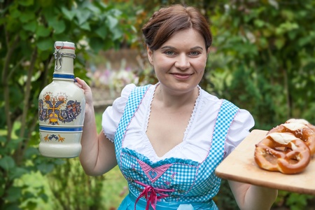 Young beautiful girl in dirndl dress holding Oktoberfest pretzel and beer mug in handsの写真素材