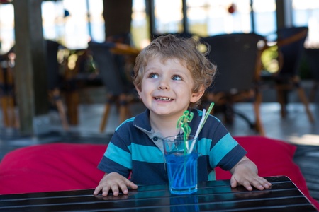 Adorable toddler boy boy sitting on high chair in cafe with cocktail on sunny summer dayの写真素材
