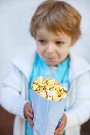 Happy little boy with popcorn bag, eating sweets. Selective focus on popcorn bagの写真素材
