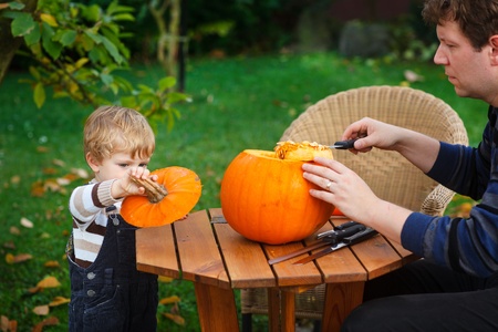 Young man and toddler boy making jack-o-lantern for halloween in autumn gardenの写真素材