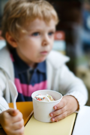 Adorable little boy eating frozen yoghurt ice cream in city cafe. Selective focus on ice creamの写真素材