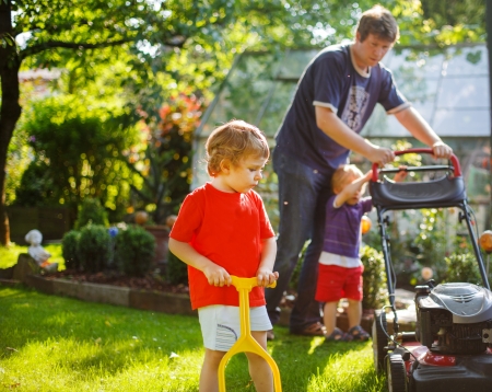 Man and two little sibling boys having fun with lawn mower in gardenの写真素材
