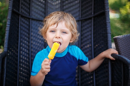 Little blond boy eating yellow ice cream in summerの写真素材