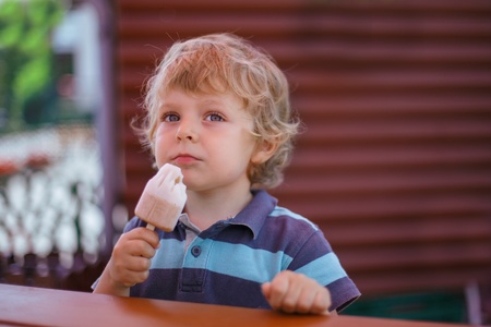 Little blond boy eating yellow ice cream in summerの写真素材