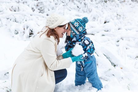 Young mother and little toddler boy having fun with snow outdoors on beautiful winter dayの写真素材