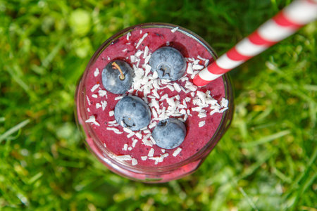 Fresh smoothie drink with different berries as healthy breakfast. On green grass background
