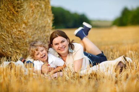 Young mother and little toddler boy having fun at picnicking on yellow hay field in summerの写真素材