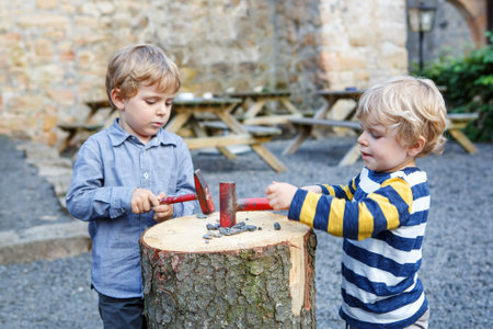 Two little sibling boys playing with hammer outdoorsの写真素材
