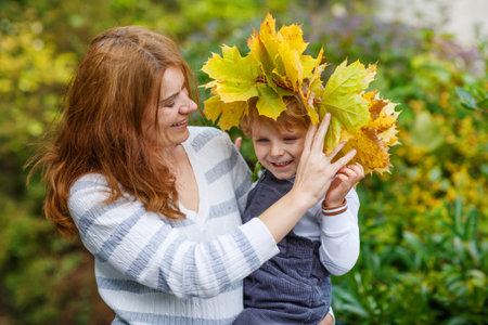 Young  mother in a maple leaf wreath holding little toddler boy in autumn parkの写真素材