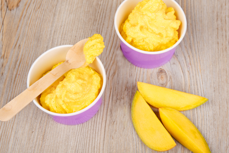 Serving of frozen homemade creamy ice yoghurt  with fresh mango and wooden spoonの写真素材